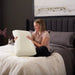 Woman sitting on a bed holding the Malouf Zoned Talalay Latex Pillow core